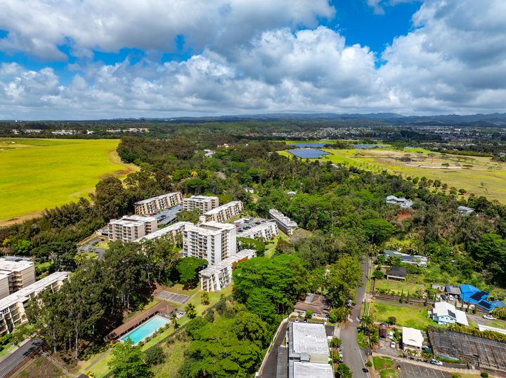 Aerial view of Central Oʻahu condos among green trees and open fields with mountains on the horizon